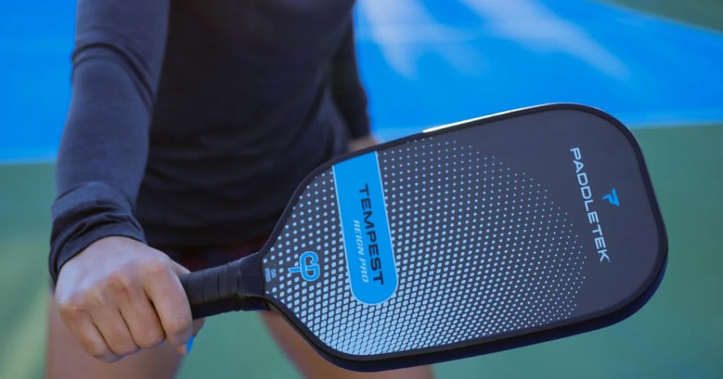 Cận cảnh bàn tay cầm cán vợt Paddletek Tempest màu xanh trên sân